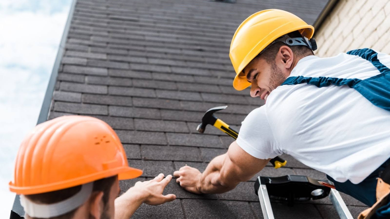 Two men in hard hats working on a roof repair.