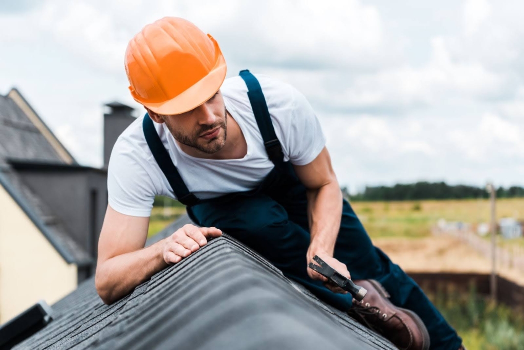 Man in a hard hat on a roof and holding a hammer.