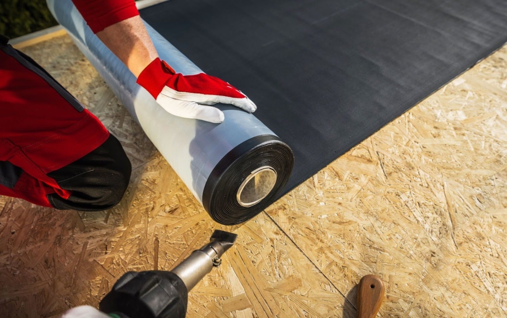 A roofer rolls out the EPDM membrane during residential flat roof installation.