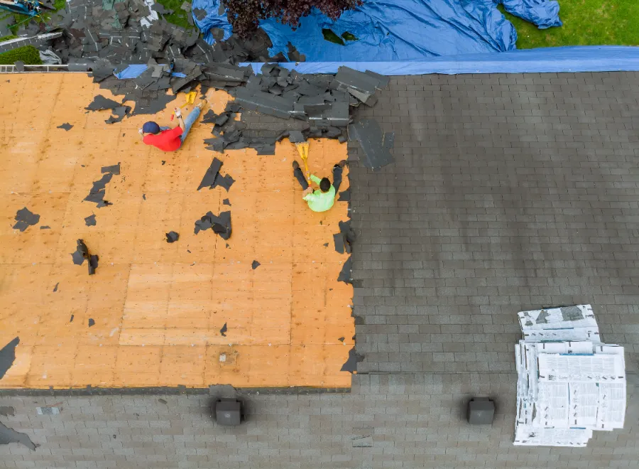 A team of workers remove old shingles during a commercial roof replacement.